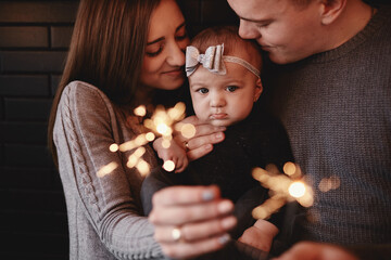 portrait of happy family, mom, dad and baby girl with sparklers and light. family in anticipation of Christmas. selective photo.