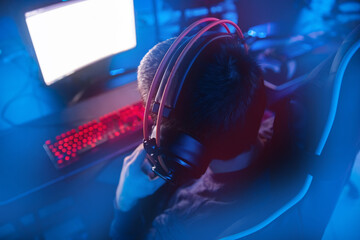Background professional gamer playing tournaments online games computer with headphones, red and...