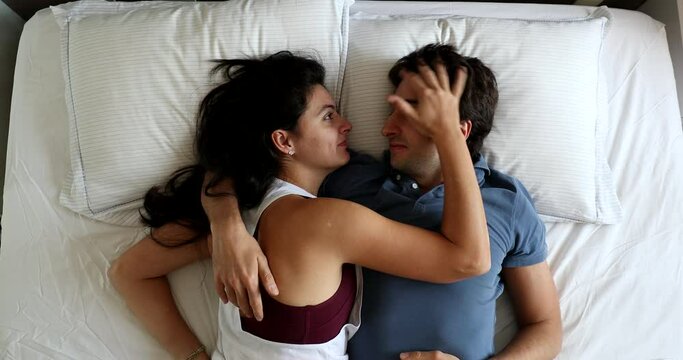 Young couple in bed in the morning talking in conversation, top view