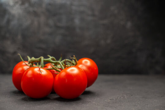 Side view fresh red tomatoes with stems on dark background in horizontal view