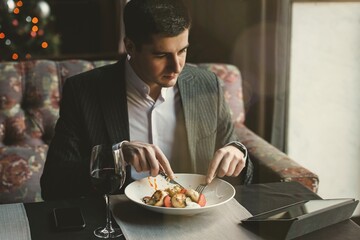 A young attractive man eating cottage cheese pancakes with sour cream and almond flakes and sea buckthorn-orange sauce in an indoor restaurant