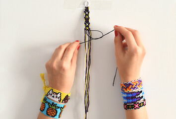 Process of weaving knot for DIY friendship bracelet. Female hands with many handmade bracelets on...