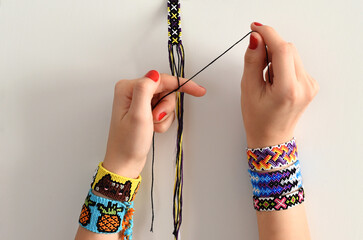 Process of weaving knot for DIY friendship bracelet. Female hands with many handmade bracelets on...