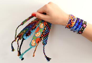 Female hand holding woven multi-colored DIY friendship bracelets handmade of embroidery thread with knots