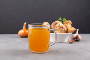 Homemade boiled beef bone broth in mug on grey table, dark  background. Golden meat bouillon. Bones...