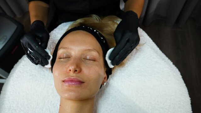 a master beautician in black rubber gloves runs two swingers over the patient's face