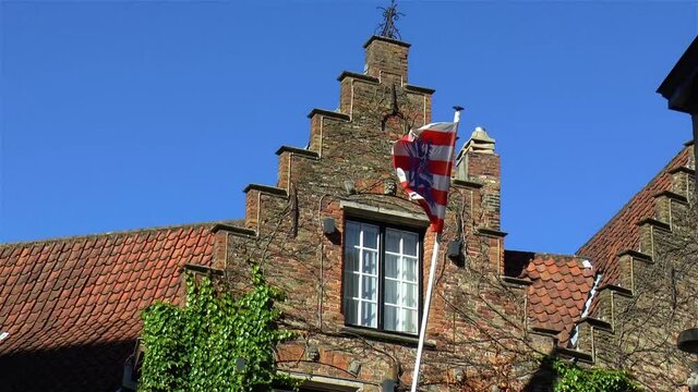 Flag of the City of Bruges, in West Flanders, Belgium, waving at traditional house façade.