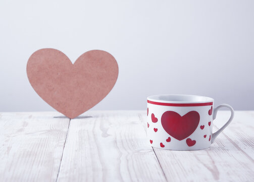 a cup with a picture of a heart on a background of a heart made of plywood on a table made of white wooden boards
