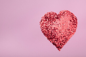 Heart shape made of red glitter on pink background. Love concept.