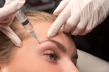 Woman getting cosmetic injection of botulinum near eyes. Crow's feet wrinkles. Eyebrow mesotherapy.