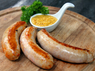 Grilled pork sausages with mustard on a wooden plate