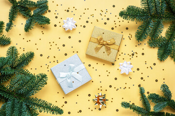 Two gifts and green fir branches on a yellow background with confetti. Christmas concept. Top view, flat lay, copy space