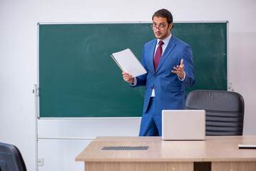 Young male teacher in suit in front of green board