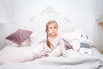 Little girl in a pink dress sits on the bed and hides something behind her back