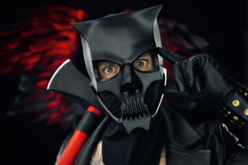 a man in a demon skull mask in a leather cloak with an axe on a background of black and red wings