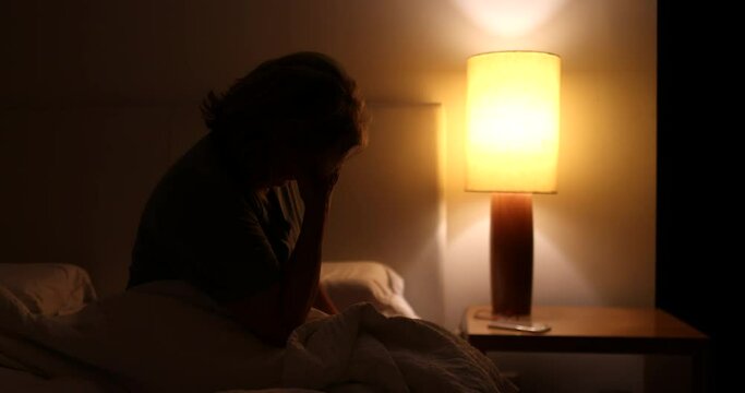 Anxious woman sitting by the bed side unable to sleep. Sleepless person in worry at night