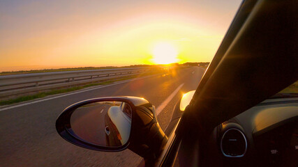 CLOSE UP Summer evening sun rays shine on a sportscar driving down empty freeway
