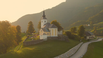 AERIAL: Catholic church is illuminated by the golden summer evening sunbeams.