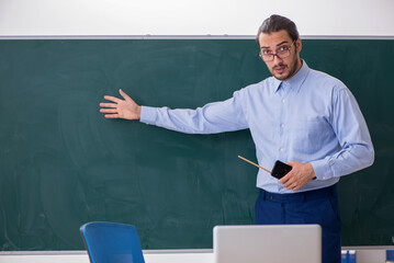 Young male teacher in the classroom in front of green board