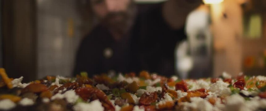 Italian chef sprinkles toppings over traditional al taglio pizza, slow motion,shallow depth of field