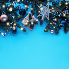 Fir branches, gift in a box and baubles on blue background with Christmas lights. Top view, flat lay, copy space