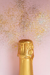 Golden Champagne bottle and glitter on pink background