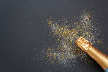 Top view of champagne bottle and glitter on black background with copy space. Celebration concept