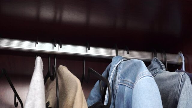 Young man hangs hanger with blue denim jacket in wardrobe, close up