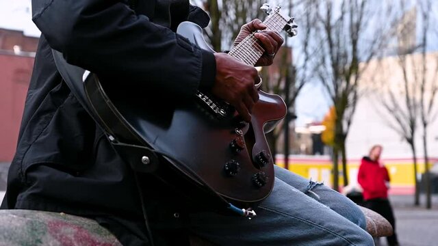 Side view close up of black man playing guitar outdoors. Slow motion.
