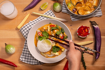 red curry with jasmine rice on a pine table with ingredients spread on the table 