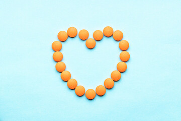 empty heart symbol formed orange pills or tablets isolated on a blue background. above view. outer space. cardiac medicine concept