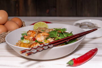 pad thai noodles with tofu and prawns in a white plate on a old white wooden table