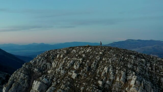Aerial view around a man walking on a rocky mountain ridge, during sunset, in Cilento and Vallo di Diano national park, Salerno, Italy - orbit, drone shot