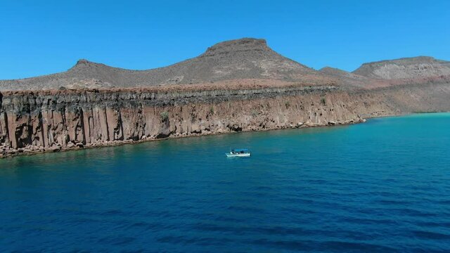 Aerial view Panning shot, a tourist boat park beside the Isla Espiritu Santo in Baja Sur, Mexico, scenic view of deep blue sea  and mountain range in the background.