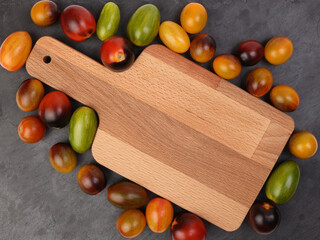 Red orange yellow green tomato mix variety on around wooden chopping board frame copy text space over black slate stone background