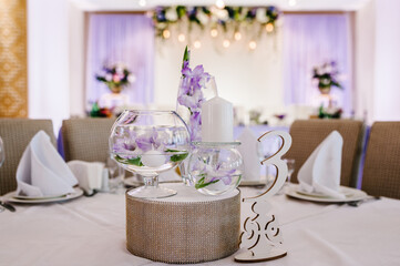 Festive table decorated with composition of violet, purple, pink flowers and greenery, candles in the banquet hall. Table newlyweds in the banquet area on wedding party.