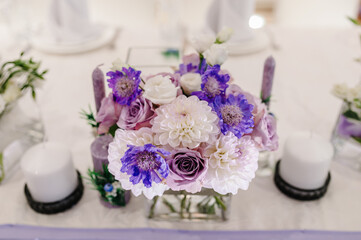 Festive table decorated with composition of violet, purple, pink flowers and greenery, candles in the banquet hall. Table newlyweds in the banquet area on wedding party.