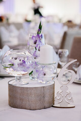 Festive table decorated with composition of violet, purple flowers and greenery, candles in the banquet hall. Table newlyweds in the banquet area on wedding party.