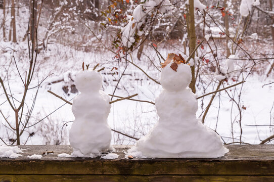 Two miniature snowmen, depicting a boy and girl on a wooden railing in Frick Park on a winter day in Pittsburgh, Pennsylvania, USA