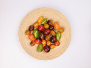 Red orange yellow green tomato mix variety on wooden plate over white background