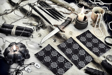 Styled still life with back of tarot cards, black candles, ritual knife and runes on witch table.