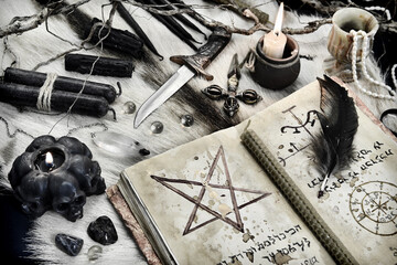 Styled still life with black magic grimoire book, burning candles and ritual objects on witch table