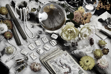 Styled still life with tarot cards deck, magic crystal, runes, candles and flowers on witch table.