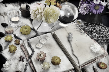 Styled still life with old book, runes, healing herbs and ritual magic objects on witch table.