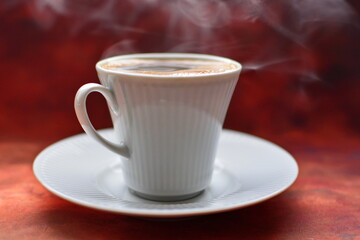 Full to the brim white coffee cup on white porcelain saucer strong black invigorating coffee with foam and thick aromatic smoke on brown background. Side view