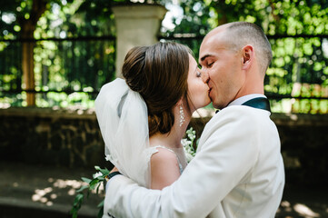 The first meeting is newlyweds in a green park outdoors. Bride kissing groom, surprise in nature. Happy wedding day of marriage.