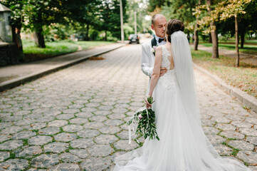 The bride and groom with a wedding bouquet, kissing and standing in the park.