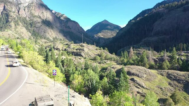Aerial Drone Rising Motion of Cars Driving with Roof Racks on Highway 550 Through Ouray Colorado Mountains Surrounded by Thick Pine Tree Forest and Power Lines