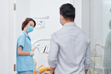 Smiling dental nurse inviting patient in office and asking him to sit in dental chair