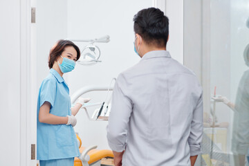 Fototapeta premium Smiling dental nurse inviting patient in office and asking him to sit in dental chair